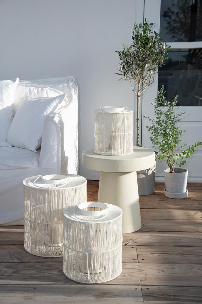 Huiselijk sfeerbeeld van het prachtige basic tafeltje gecombineerd met 3 metalen windlichten, een witte bank en wat groene planten | Conceptstore Sisällä